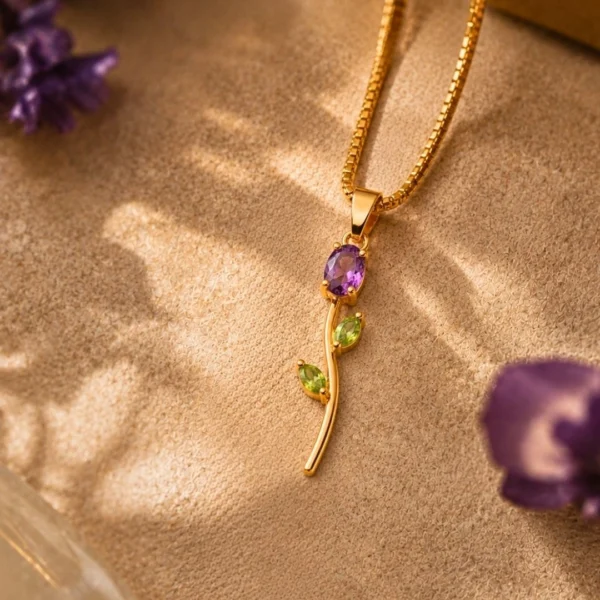 Gold floral pendant necklace with purple and green gemstone accents on a textured beige background