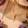 Gold floral pendant necklace with purple and green gemstone accents on a textured beige background