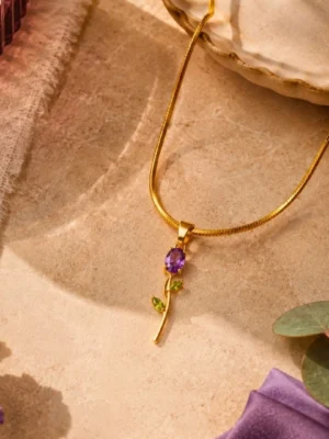 18K gold-plated floral pendant necklace with purple and green gemstones for women Gold floral pendant necklace with purple and green gemstone accents on a textured beige background