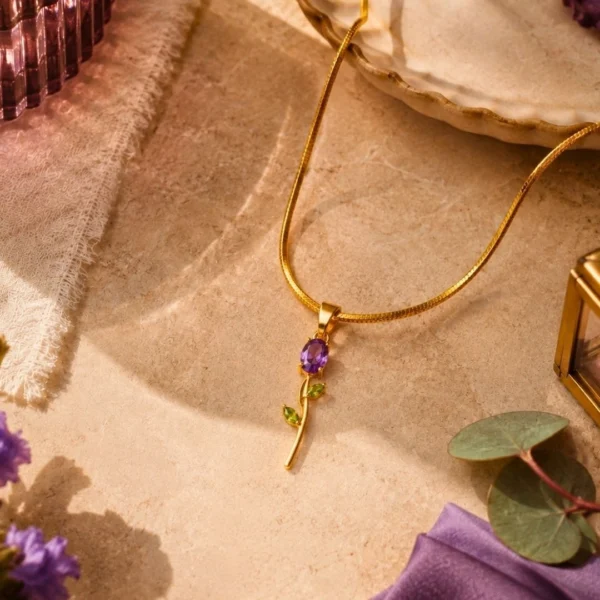 Gold floral pendant necklace with purple and green gemstone accents on a textured beige background