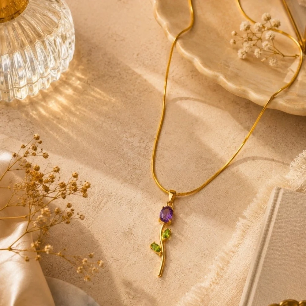 Gold floral pendant necklace with purple and green gemstone accents on a textured beige background