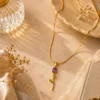 Gold floral pendant necklace with purple and green gemstone accents on a textured beige background
