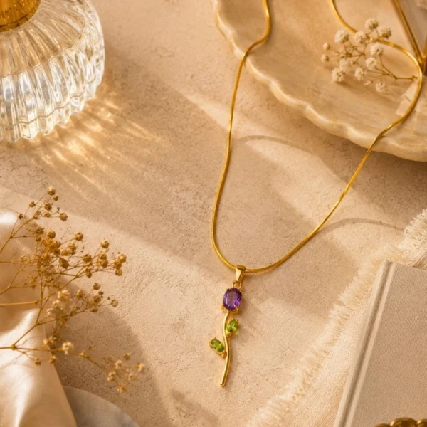 Gold floral pendant necklace with purple and green gemstone accents on a textured beige background